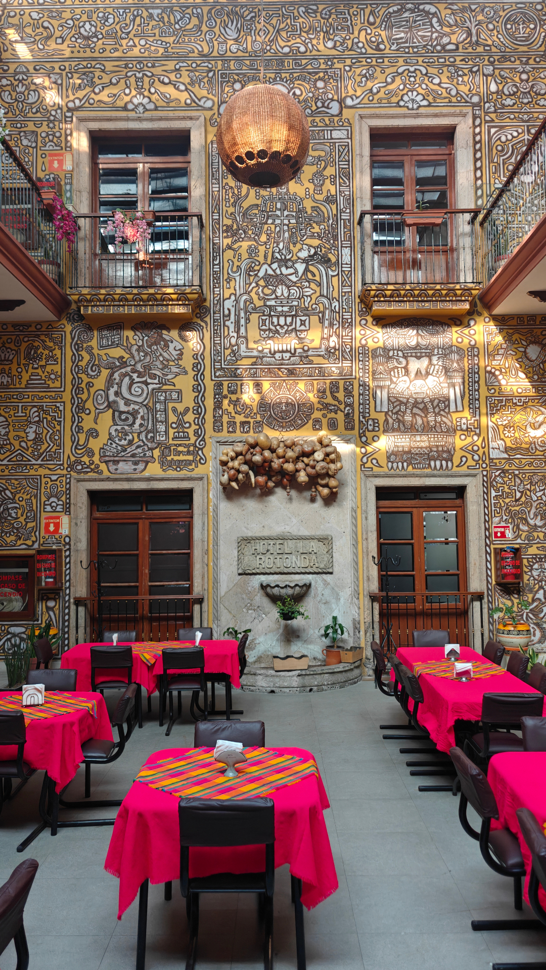 Comedor con mural maya en muros amarillos y mesas con mantel rosa